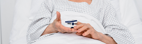Cropped view of elderly patient holding oximeter on bed in clinic, banner