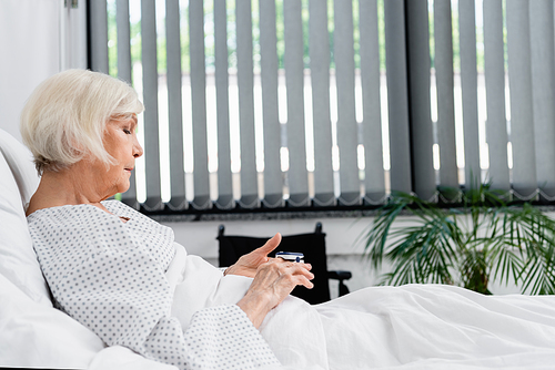 Side view of elderly patient using oximeter on hospital bed