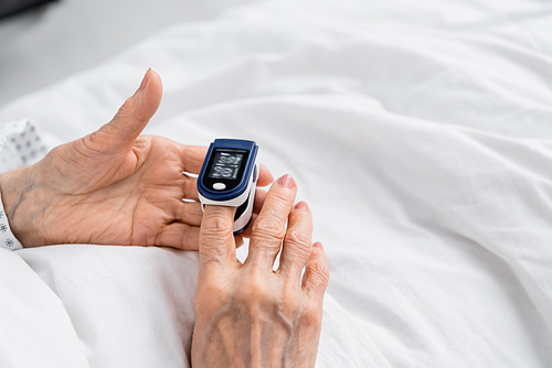 Cropped view of elderly patient using digital oximeter on hospital bed