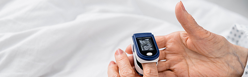 Cropped view of elderly woman using digital oximeter on hospital bed, banner