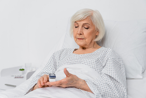 Senior woman using digital oximeter on blurred foreground in hospital