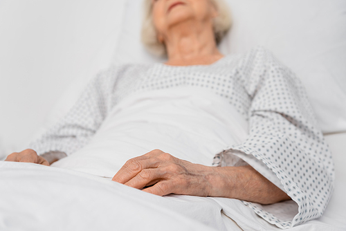 Cropped view of senior woman lying on bed in hospital ward