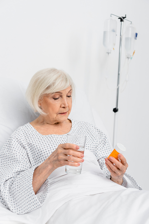 Elderly patient holding pills and glass of water in hospital ward