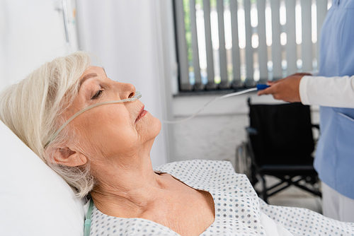 Side view of senior woman with nasal cannula near blurred african american nurse in hospital