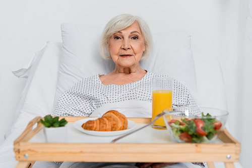 Elderly patient looking at camera near blurred food in hospital ward
