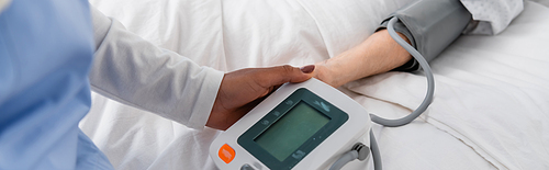 Cropped view of african american nurse holding tonometer near woman on hospital bed, banner