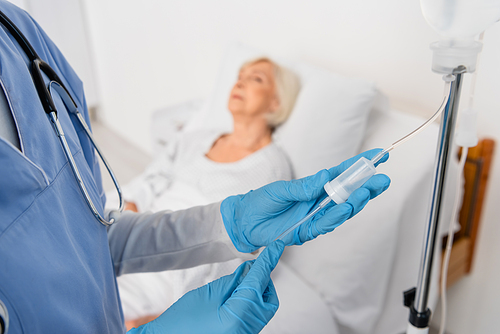Nurse in latex gloves standing near intravenous therapy station in hospital ward