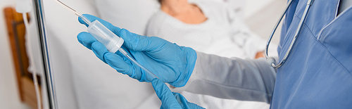 Cropped view of nurse holding tube of intravenous therapy station in hospital ward, banner