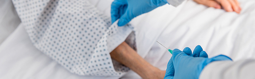 Cropped view of nurse holding catheter near senior patient on blurred background, banner