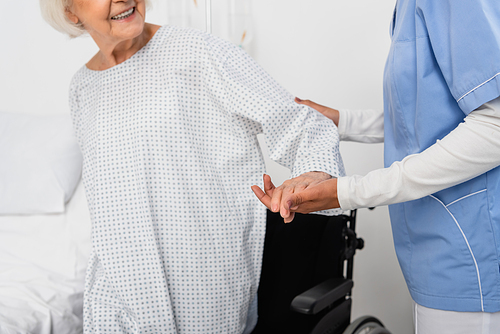 Cropped view of african american nurse holding hand of smiling woman on blurred background