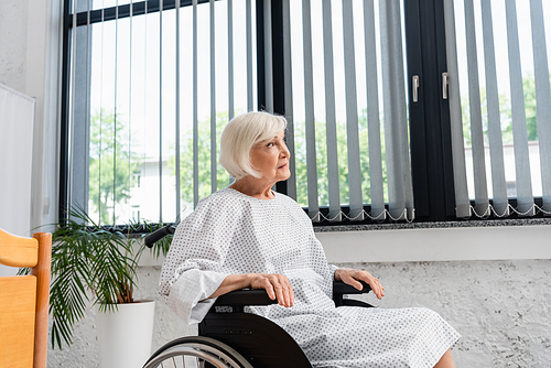 Elderly woman in wheelchair looking away in hospital ward