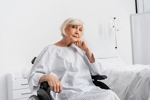 Senior woman in patient gown sitting in wheelchair