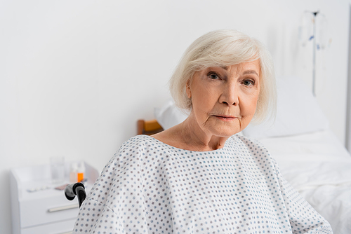 Senior woman in patient gown looking at camera in wheelchair