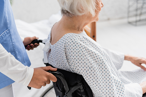 Cropped view of african american nurse standing near senior patient in wheelchair