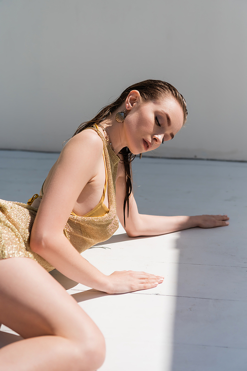 young woman in golden summer dress lying on white surface