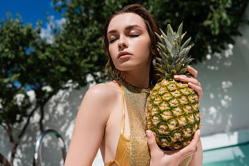 low angle view of young woman with closed eyes holding ripe pineapple outside