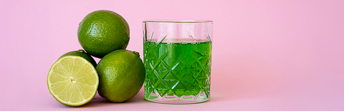 green alcohol drink in glass near fresh and organic limes on pink, banner