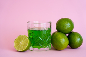 green fresh limes near alcohol drink in faceted glass on pink