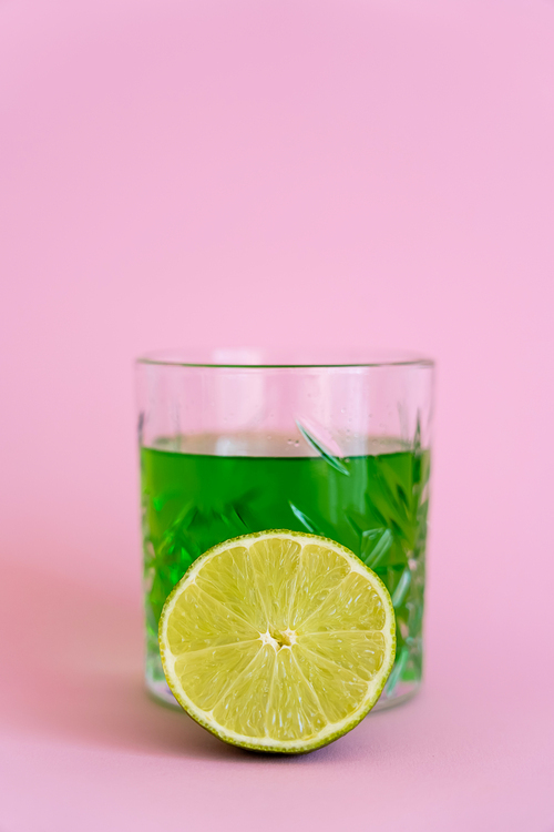 green fresh lime near alcohol drink in glass on pink