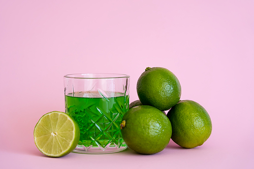 green liquid in glass near fresh limes on pink background