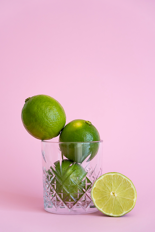 green fresh citrus fruit in faceted glass near half of lime on pink