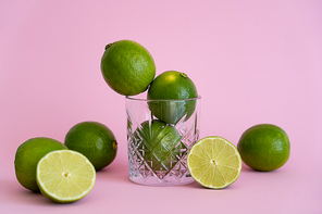 green fresh citrus fruit in faceted glass near halves of limes on pink background