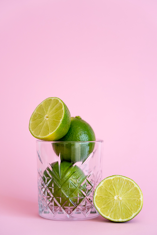green and fresh limes in faceted glass on pink background