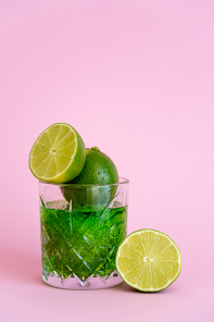 green and fresh limes in faceted glass with sparkling alcohol drink on pink