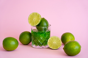 green and fresh limes in faceted glass with alcohol drink on pink