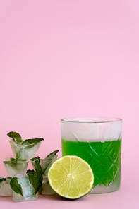 green and fresh lime in faceted glass with alcohol drink near ice cubes with peppermint on pink