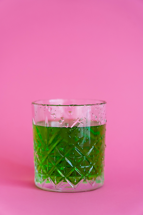 green alcohol drink in faceted glass with water drops on pink