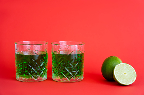 green alcohol drink in faceted glasses with water drops near limes on red