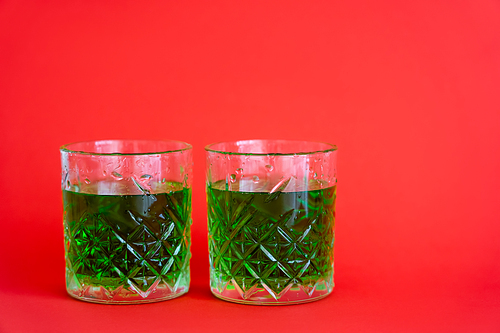 green alcohol drink in faceted glasses with water drops on red