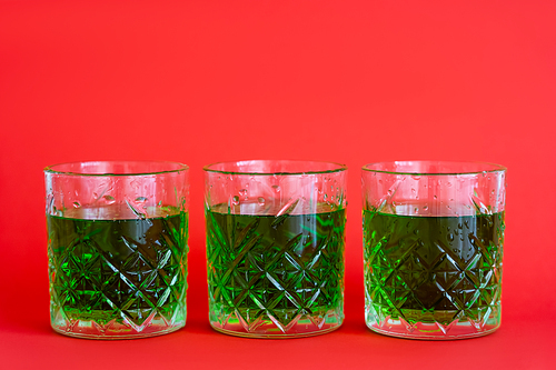 green alcohol drink in three faceted glasses with water drops on red