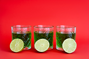 green alcohol drink in three faceted glasses with water drops and halves of limes on red