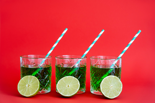green alcohol drink in faceted glasses with straws and halves of limes on red