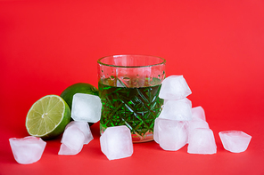 frozen ice cubes near glass with alcohol green mojito and limes on red