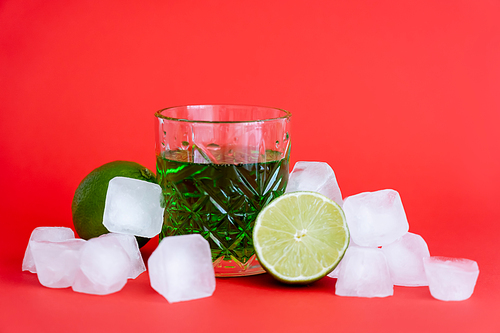 frozen ice cubes near glass with alcohol green drink and limes on red