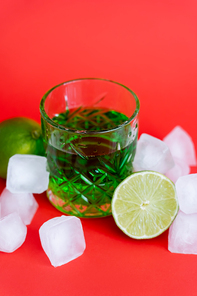 frozen ice cubes in glass with alcohol green beverage and limes on red