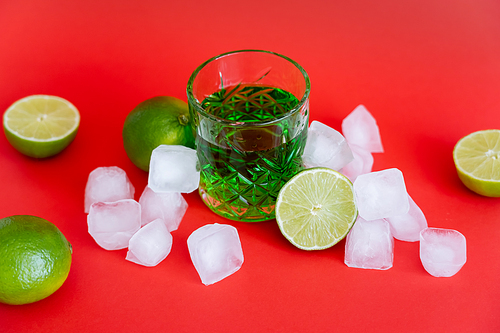 frozen ice cubes near glass with alcohol mojito and fresh limes on red