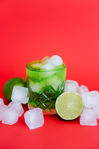 frozen ice cubes in glass with alcohol green mojito and limes on red