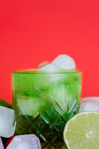 close up of frozen ice cubes in glass with sparkling green mojito and limes on red