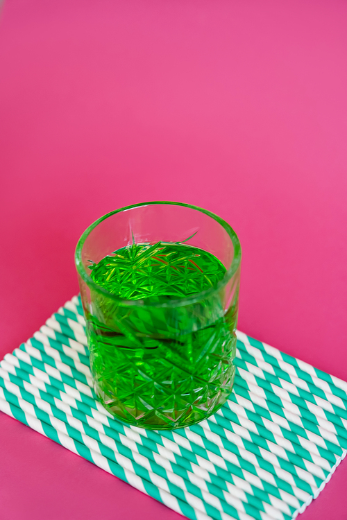 high angle view of glass of green alcohol drink on striped paper straws on pink