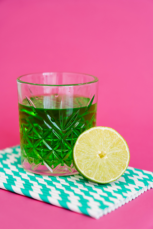 glass of green alcohol drink on striped paper straws near sour lime on pink