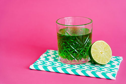 glass of green alcohol drink on striped paper straws near sliced lime on pink