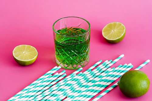 glass of green alcohol drink near striped paper straws on pink