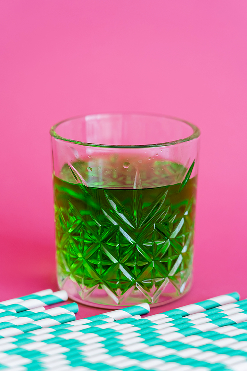 striped paper straws near faceted glass with green cocktail on pink