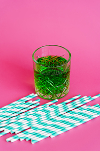 striped paper straws near faceted glass with green drink on pink