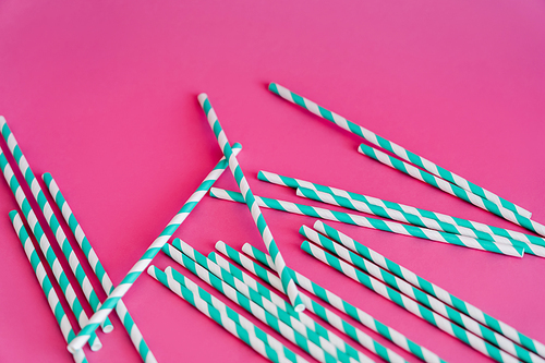 top view of striped blue and white straws on pink background