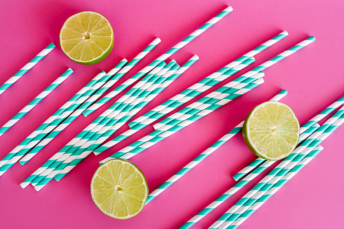 top view of striped blue and white straws near limes on pink background